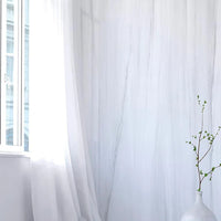 White curtains in a room with a vase and plant on a white surface.