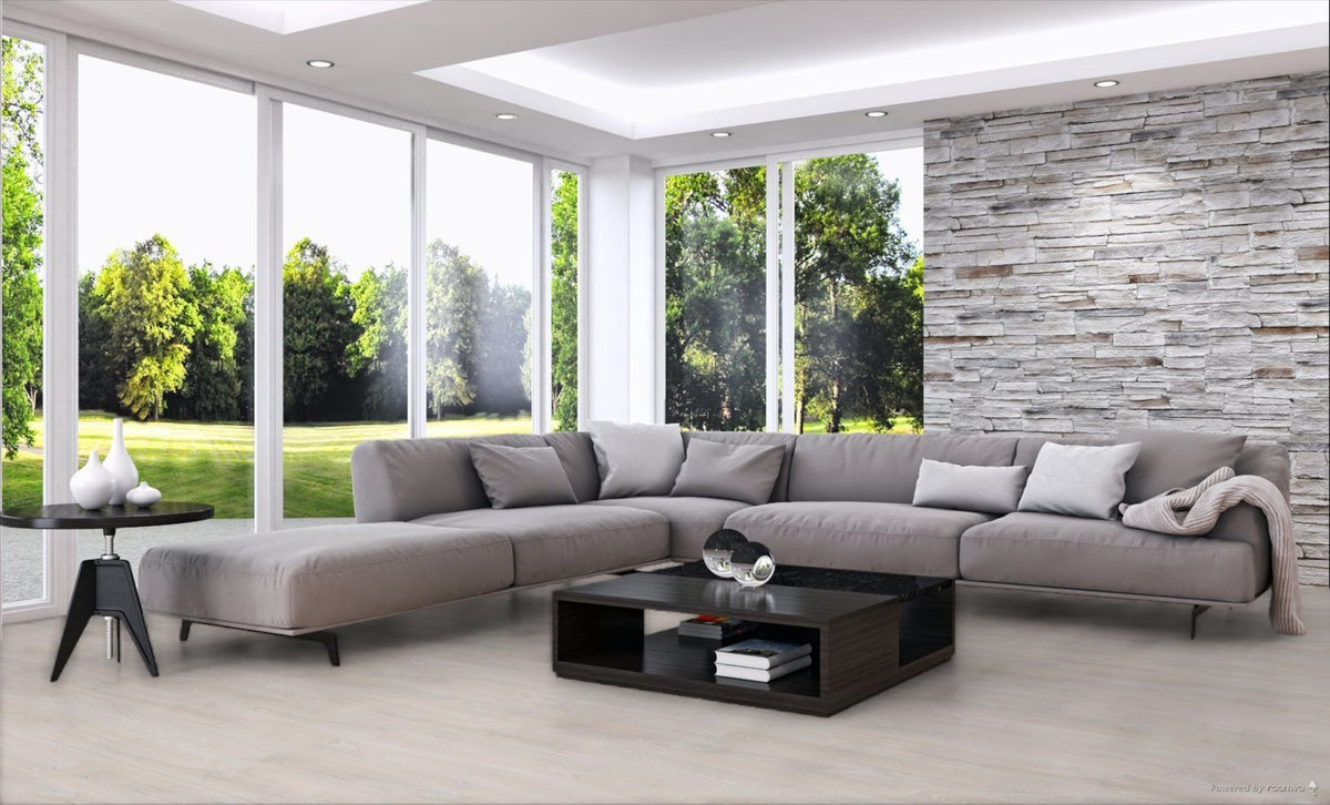 A modern L-shaped sectional sofa in light gray fabric, styled in a contemporary living room with a black coffee table, a side table, a stone accent wall, and large windows overlooking a green lawn.