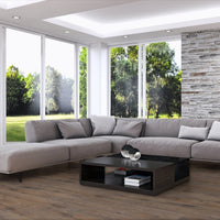 A modern light gray sectional sofa with matching throw pillows arranged in an L-shape in a bright living room with large windows, a wood-paneled accent wall, and a black coffee table.