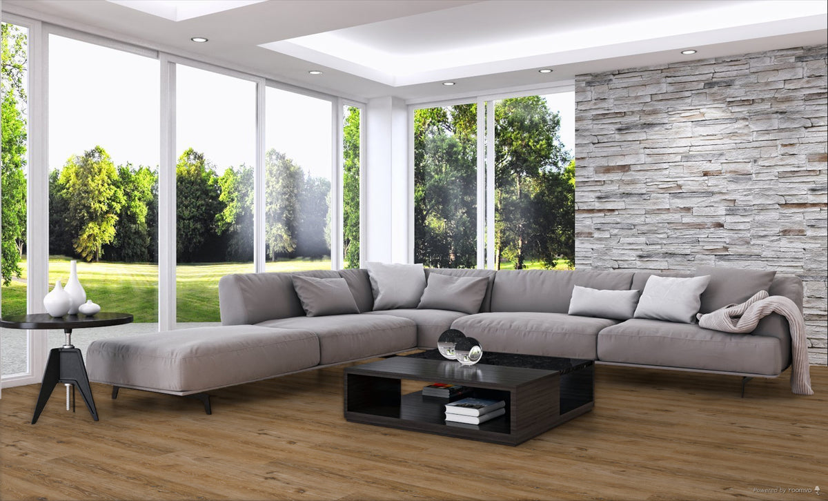 A modern light gray sectional sofa with matching throw pillows arranged in an open U-shape in a bright living room. The room features a light wood floor, a black coffee table, a textured stone accent wall, and large windows looking out onto a green lawn.
